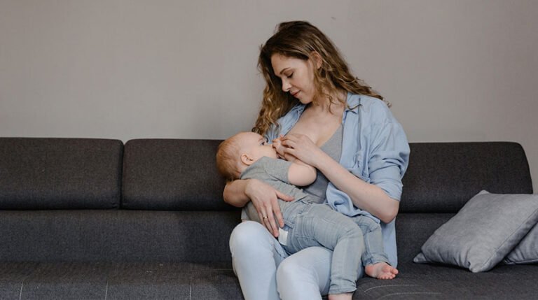 Mãe sentada no sofá amamentando bebê