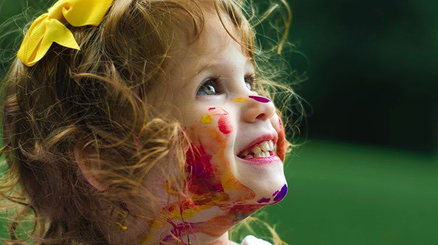 criança rindo com o rosto todo pintado de tinta