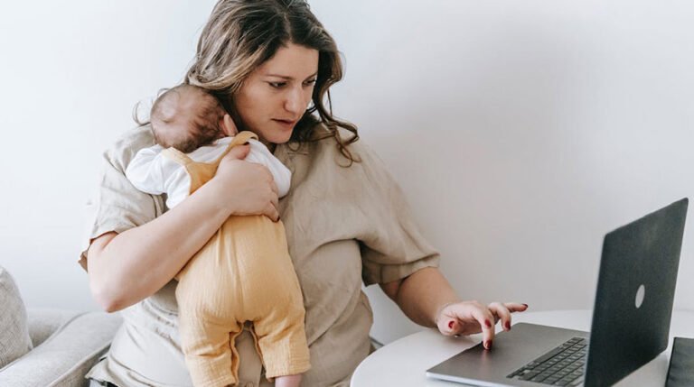 Mãe trabalhando no notebook com bebê no colo